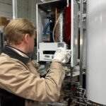 Technician installing or repairing a heating system in an indoor workshop setting.