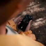 Teenage boy holds a smartphone displaying low battery outdoors in a forest.