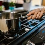 A person holding a saucepan over a gas burner in a domestic kitchen setting.
