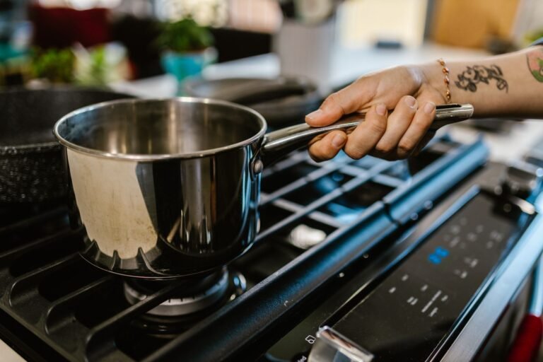 A person holding a saucepan over a gas burner in a domestic kitchen setting.
