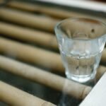 A shot glass with clear liquid placed on a bamboo surface, creating a reflective and calming scene.