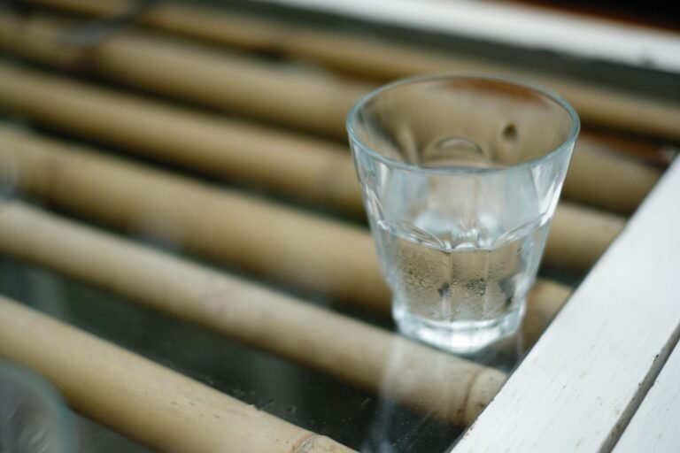 A shot glass with clear liquid placed on a bamboo surface, creating a reflective and calming scene.