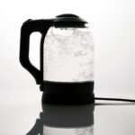 A sleek electric kettle boiling water, captured on a reflective white surface.
