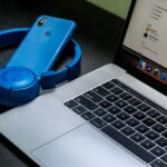 A sleek office setup featuring a laptop, blue headphones, and a smartphone, exemplifying modern technology.