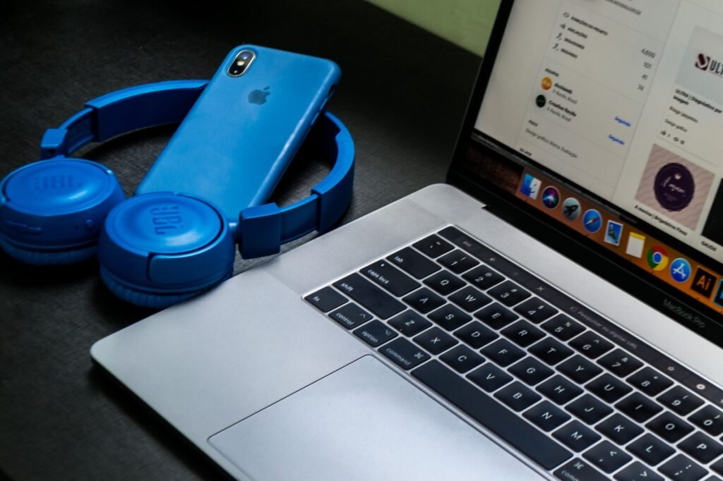 A sleek office setup featuring a laptop, blue headphones, and a smartphone, exemplifying modern technology.