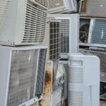 A collection of various old and broken air conditioning units piled outdoors.