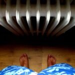 A unique perspective from above showing bare feet standing on wooden floor near a radiator.