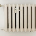 A classic white metal radiator on a plain wall, showcasing minimalist interior design.