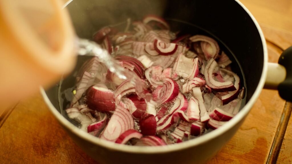 Close-up of red onions being soaked with water in a cooking pot.