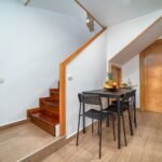 Clean and minimalist interior with wooden accents, featuring a small dining area under the stairs.