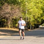 Runners participating in a marathon along a tree-lined road under a bright sunny sky.