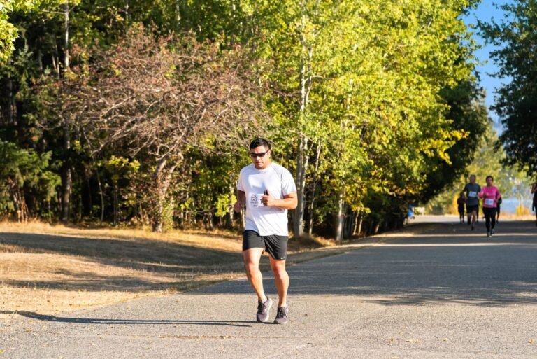 Runners participating in a marathon along a tree-lined road under a bright sunny sky.