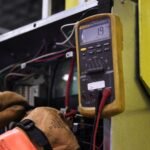 Electrician using a multimeter to fix industrial control panel wiring.