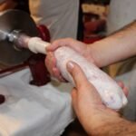 Detailed view of hands holding fresh sausage from meat stuffing machine indoors.