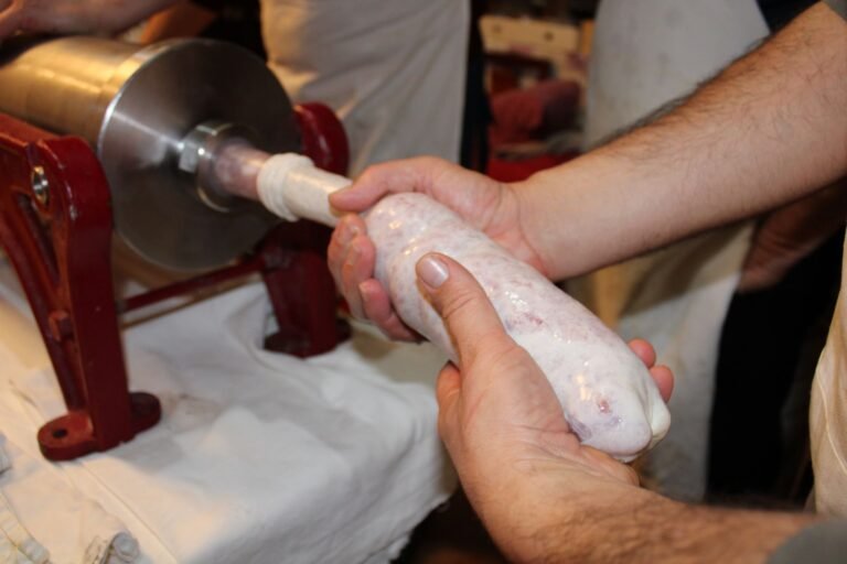 Detailed view of hands holding fresh sausage from meat stuffing machine indoors.
