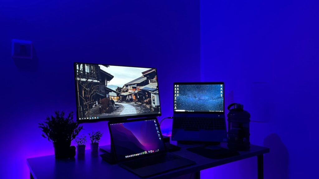 Sleek gaming desk setup with multiple screens and blue neon lighting, perfect for tech enthusiasts.
