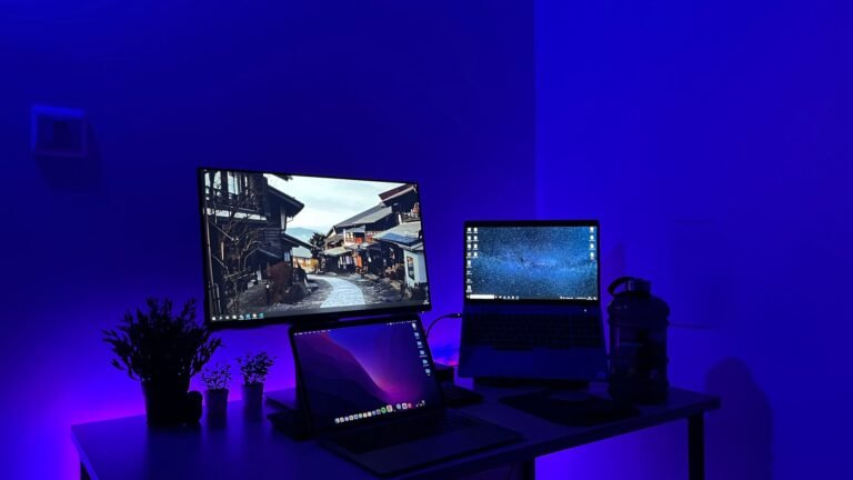 Sleek gaming desk setup with multiple screens and blue neon lighting, perfect for tech enthusiasts.
