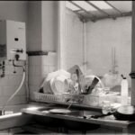 Black and white image of a kitchen sink filled with dishes and cutlery by the window.