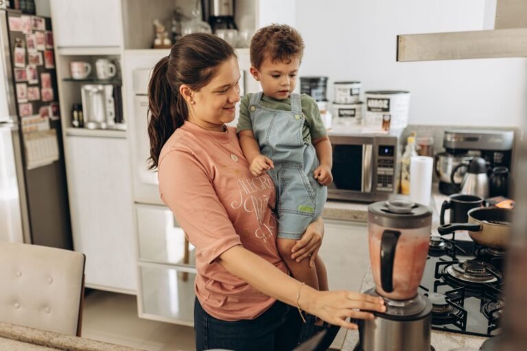 Mother and child using a blender together in a cozy kitchen setting.