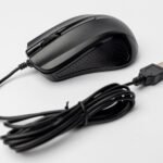 Close-up of a black wired computer mouse on a white background, showcasing its design and connection cable.