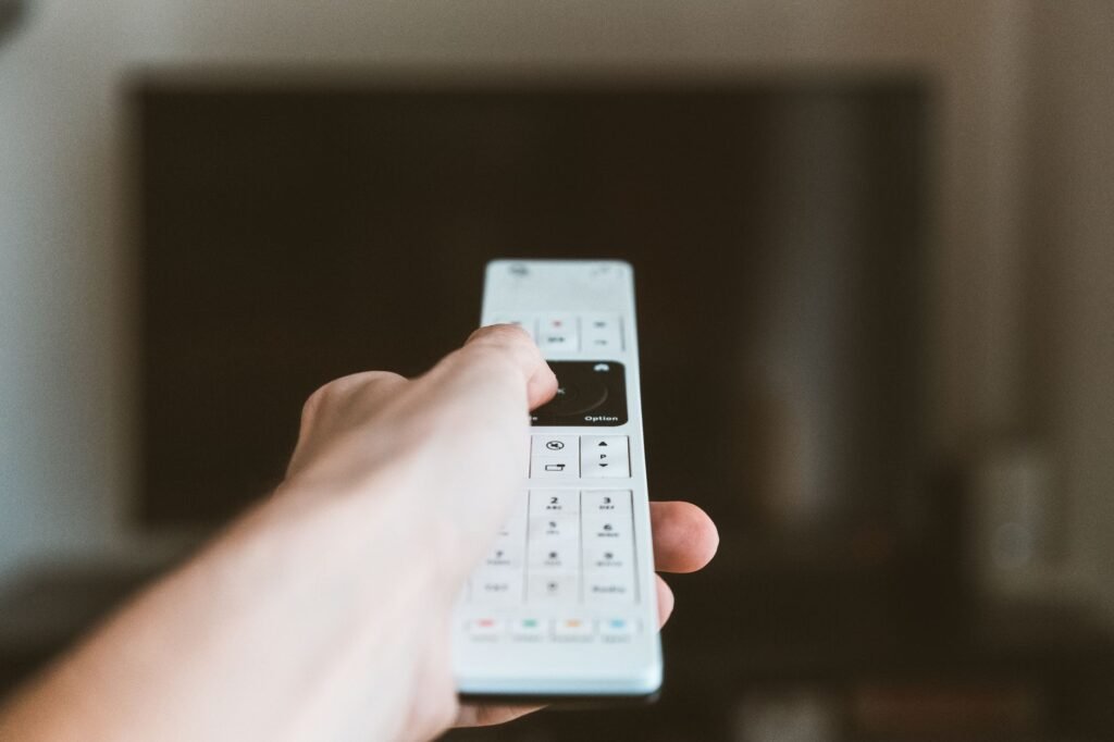 Close-up of a hand using a remote control to operate a television indoors.