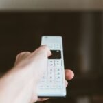 Close-up of a hand using a remote control to operate a television indoors.