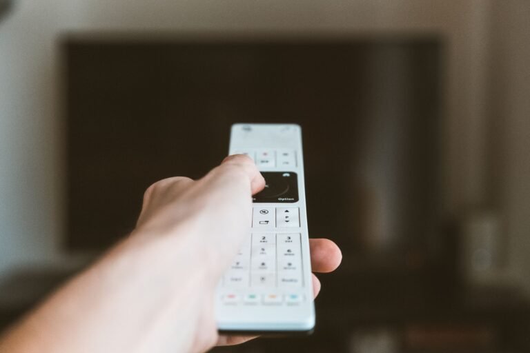 Close-up of a hand using a remote control to operate a television indoors.
