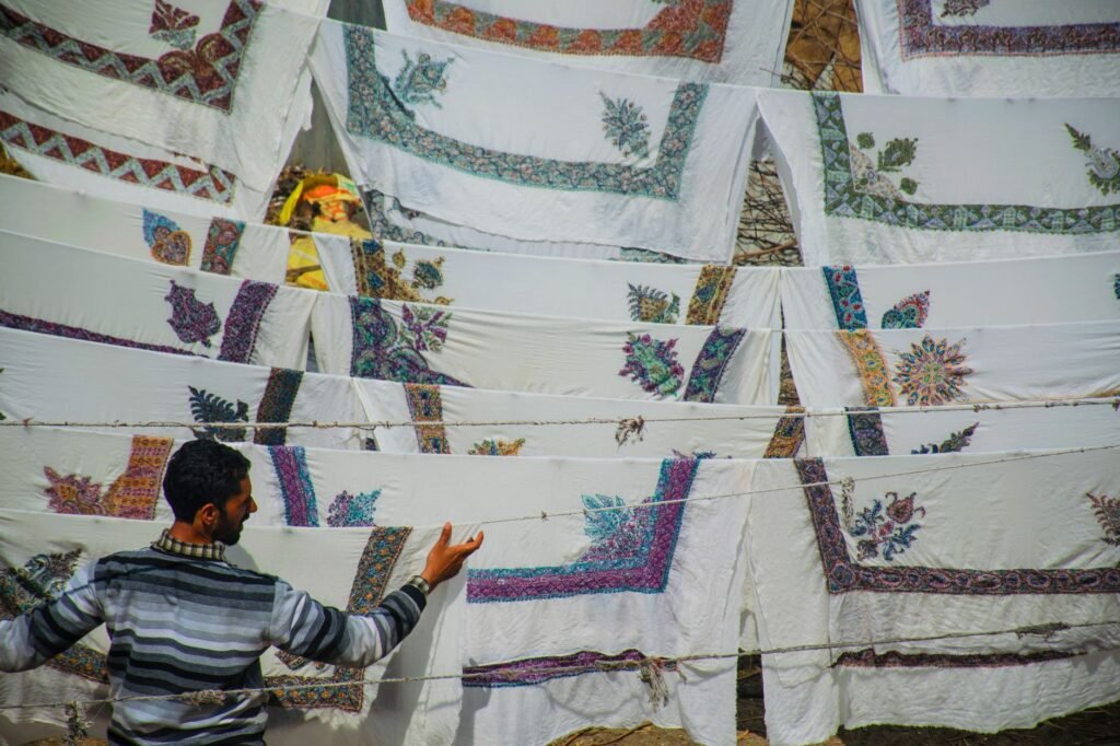 A man inspects embroidered cloths drying on a clothesline in the sun.