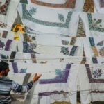 A man inspects embroidered cloths drying on a clothesline in the sun.