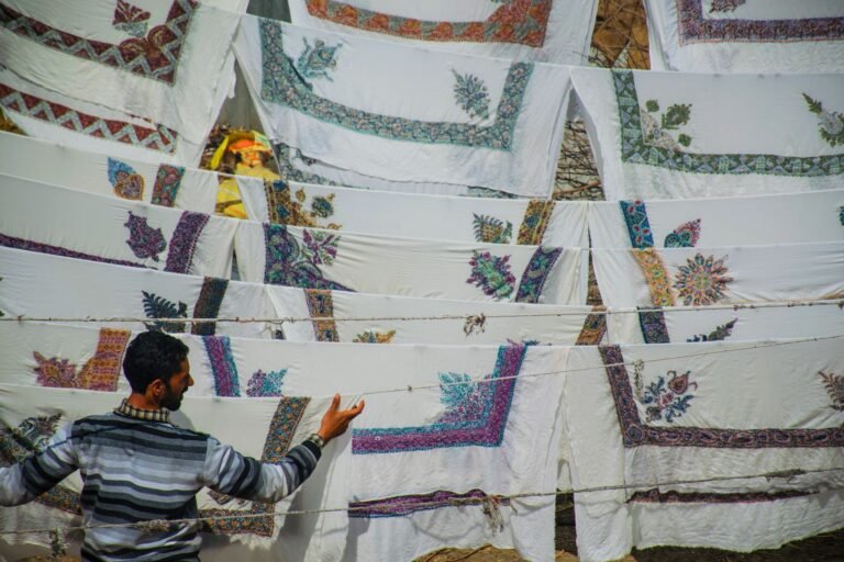 A man inspects embroidered cloths drying on a clothesline in the sun.