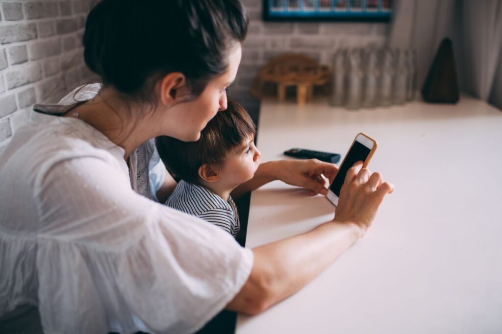 A woman and child interacting with a smartphone at home, highlighting technology and family bonding.
