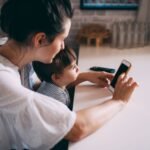 A woman and child interacting with a smartphone at home, highlighting technology and family bonding.