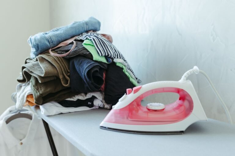 Tidy stack of clothes ready to be ironed with an iron on an ironing board.
