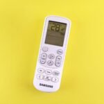 Air conditioner remote with temperature set at 28°C on a yellow background.
