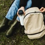 Person sitting outdoors with backpack and coffee cup, symbolizing adventure and relaxation.