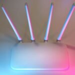 Sleek white wireless router with four antennas emitting soft blue and pink light.