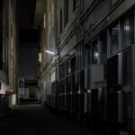 A dimly lit urban alley in Kyoto featuring air conditioning units, captured at night.