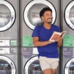 Smiling man enjoys a book while doing laundry in a Brazilian laundromat.