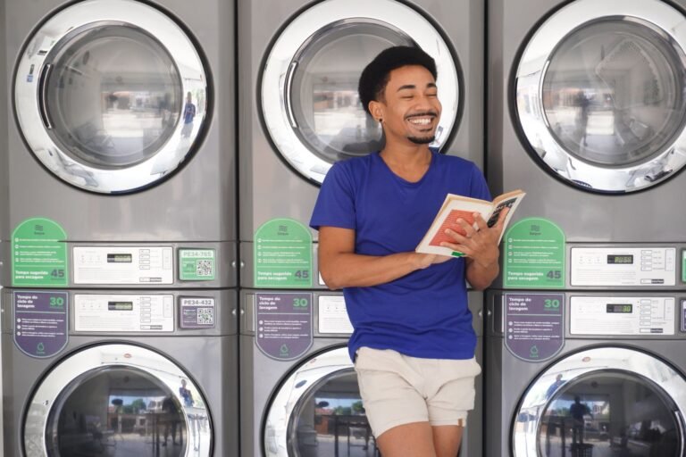 Smiling man enjoys a book while doing laundry in a Brazilian laundromat.