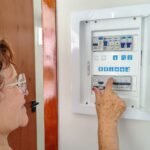 A senior woman is adjusting an electrical fuse panel indoors, demonstrating home safety.