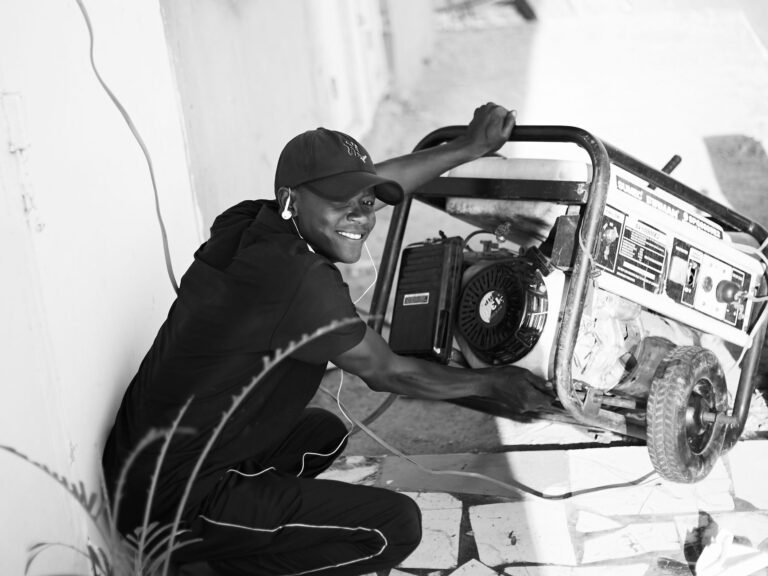 A cheerful young man wearing a cap and earphones operating a portable generator outside.