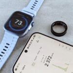 Smartwatch with fitness data, smartphone, and health ring on a gray surface.