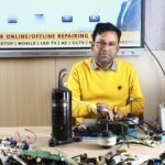 Man engages in air conditioner repair at New Delhi training center, surrounded by electronic components.