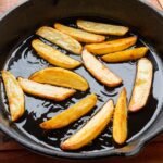 Freshly fried golden potato wedges sizzling in a cast iron skillet, showcasing delicious homemade cooking.