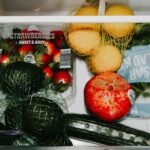 A variety of fresh fruits and vegetables including avocados, lemons, strawberries, and lettuce in a fridge drawer.