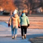 Two friends walking side by side in a winter park during sunset.