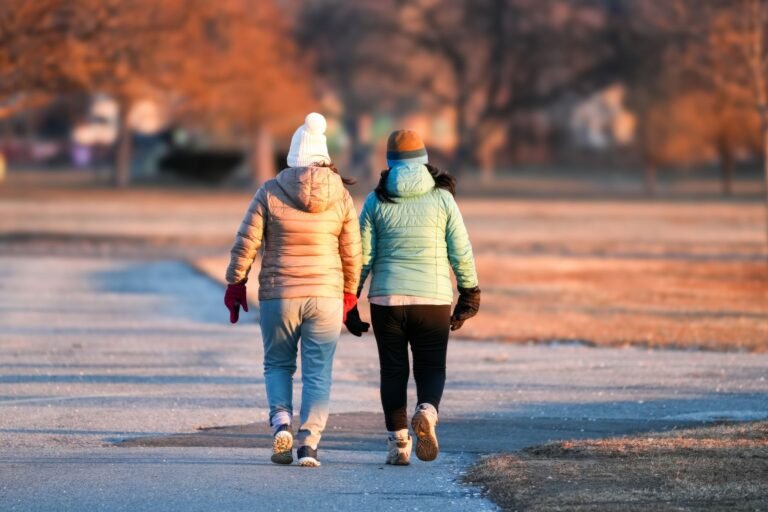 Two friends walking side by side in a winter park during sunset.
