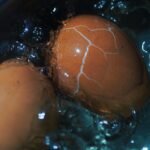 Close-up view of a cracked brown egg boiling in water, showcasing texture and cooking process.