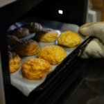 A warm, inviting scene of fresh biscuits being taken out of the oven with an oven mitt.