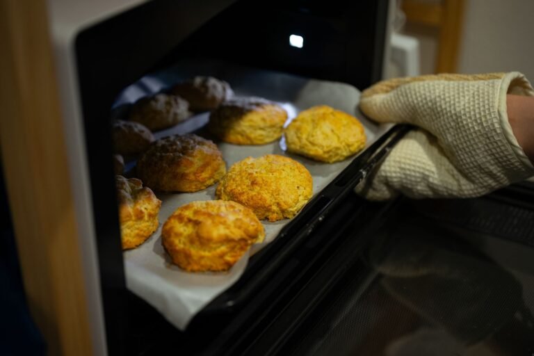 A warm, inviting scene of fresh biscuits being taken out of the oven with an oven mitt.